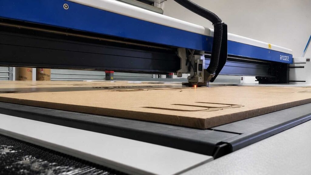 Laser Engraving for Beginners: Learn Before You Buy 4 A laser engraver head with a red light cutting designs into a large sheet of wood