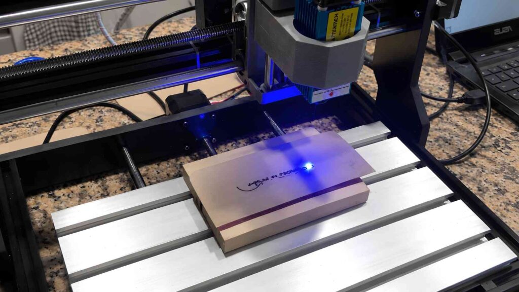 Laser Engraving for Beginners: Learn Before You Buy 2 A desktop laser engraver using a blue beam to etch a design onto a small wooden block