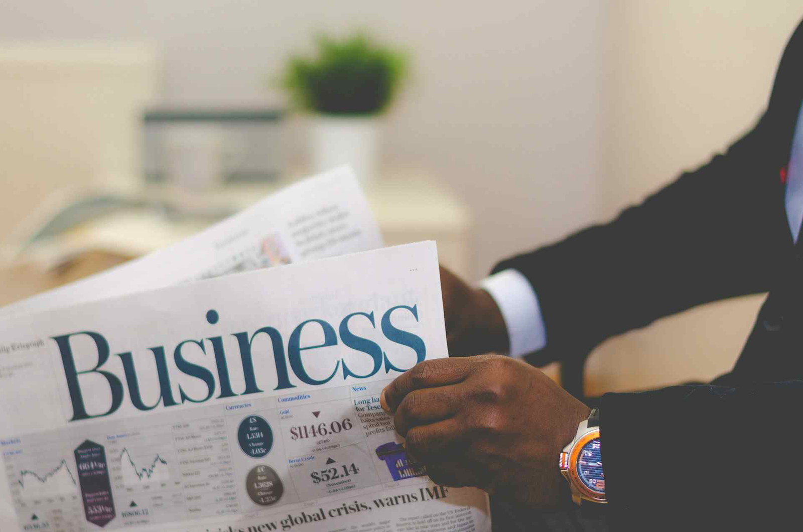 A person in a suit holding a newspaper with the headline Business and a report on a global crisis