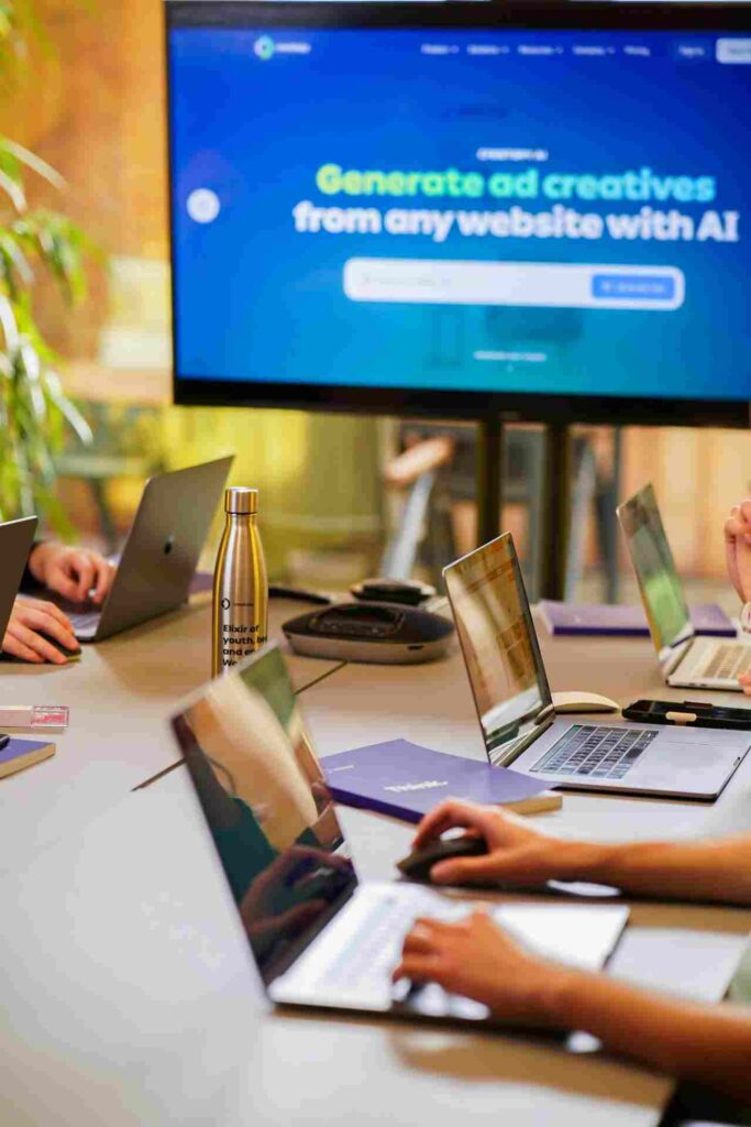 Startup Website Design in 2026: Reasons It Feels Identical 2 People working in a modern office with a large monitor displaying "Generate ad creatives from any website with AI