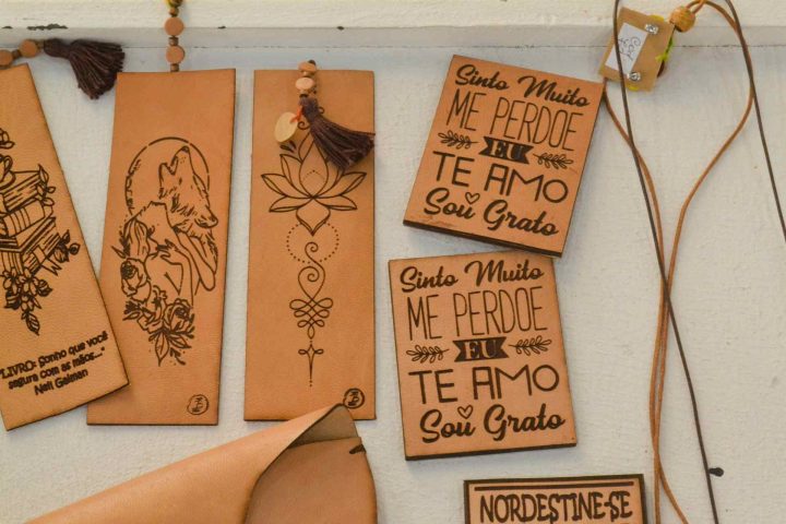 Engraved leather bookmarks and plaques featuring a wolf, lotus, and Portuguese text