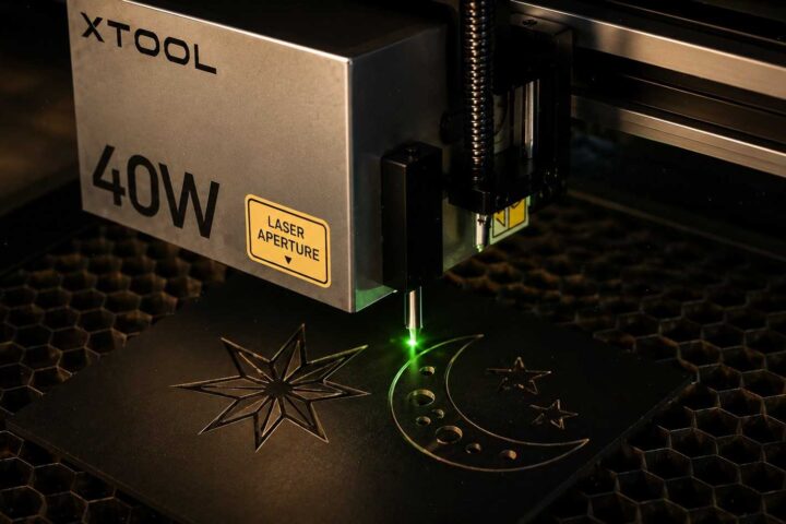xTool 40W laser engraver head with a green beam engraving celestial patterns onto a dark surface