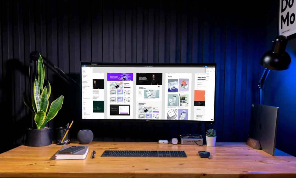 Why Clients Sometimes Choose AI Designs Over Better Custom Work 2 A large monitor on a wooden desk displaying multiple website layout mockups within a design application