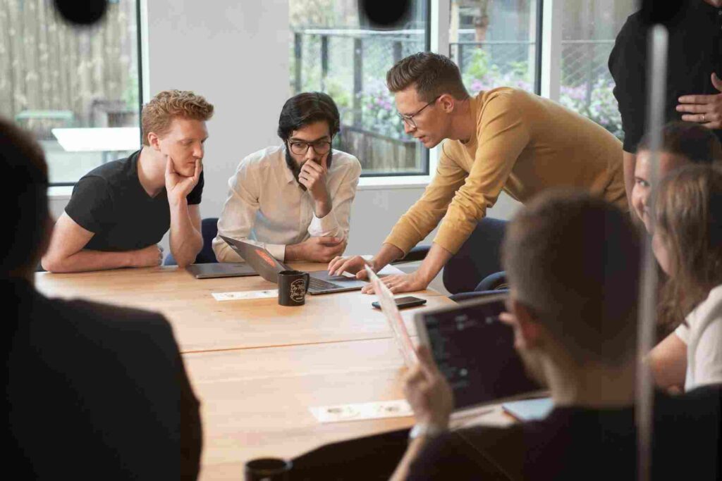 Why Clients Sometimes Choose AI Designs Over Better Custom Work 5 A man pointing at a laptop screen while explaining a project to a group of people in an office