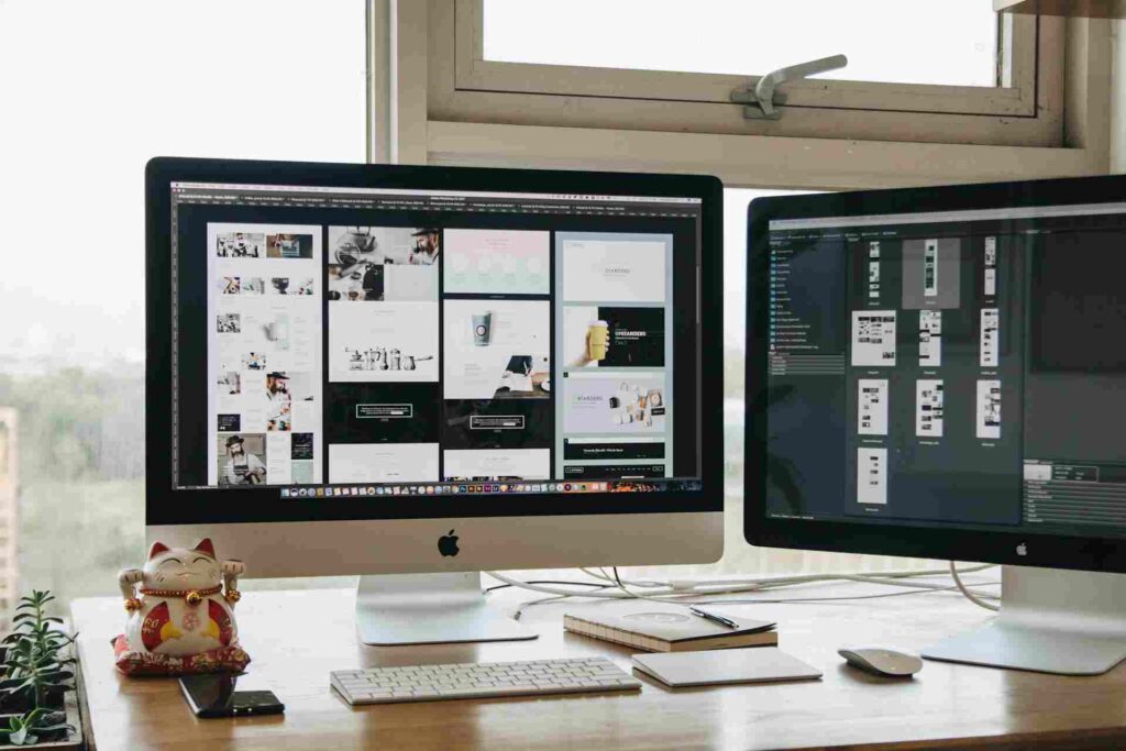 Startup Website Design in 2026: Reasons It Feels Identical 3 Two computer monitors on a desk displaying a grid of website design layouts and a graphic design interface