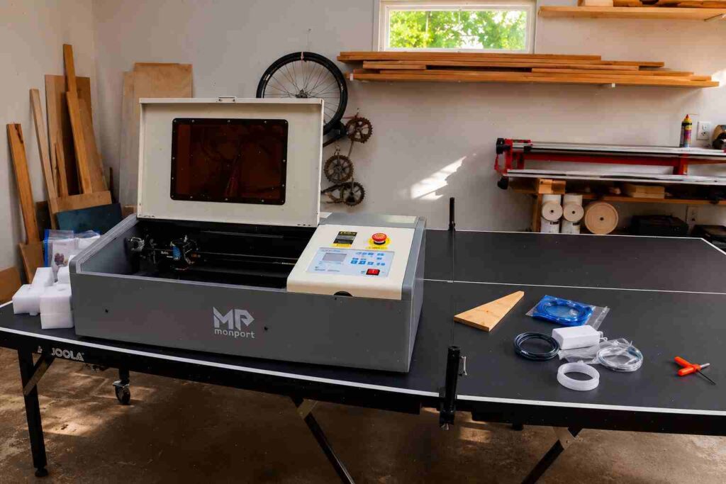 CO2 Laser Cutting Machine For Small Business: Real Setup Budget 2 Monport 40W Pro CO2 laser cutter with its lid open, sitting on a ping pong table in a garage workshop
